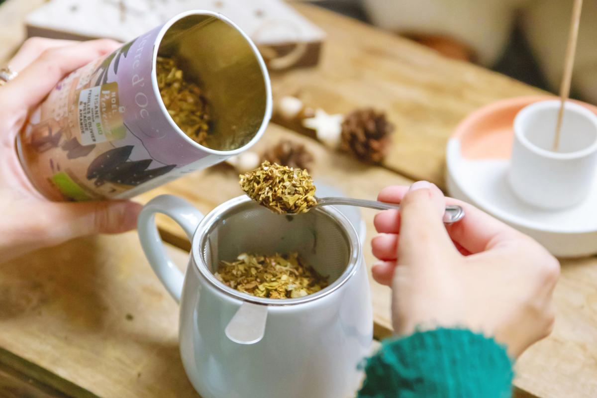 Lose Tee-Mischung, die mit einem Löffel aus einer Dose entnommen wird und in einen Teesieb einer Kanne gefüllt wird